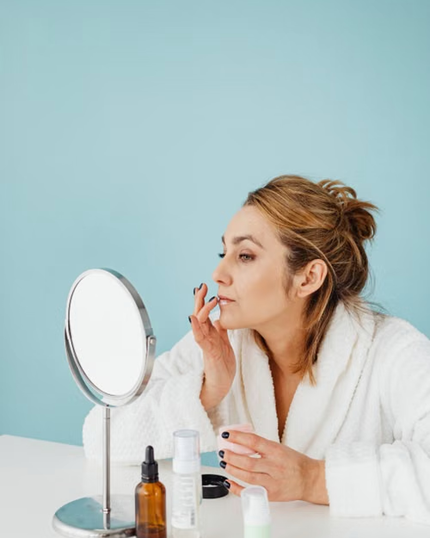 Wanita merawat kulitnya di depan cermin dengan rangkaian produk skincare